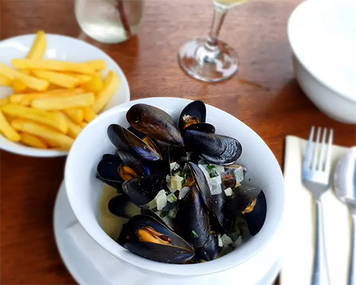 Bowl of cooked mussels and a side of French fries